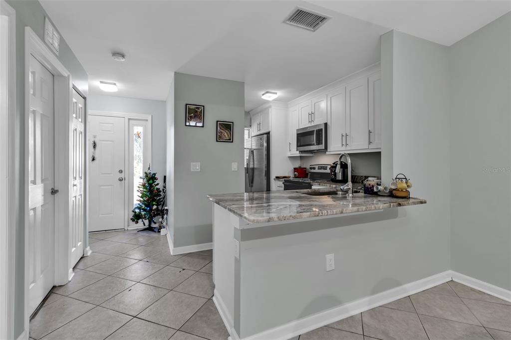 A kitchen with white cabinets and a marble-patterned breakfast bar overlooks a tiled entryway — 5370 ROYAL PALM AVENUE UNIT 5370, SARASOTA, FL