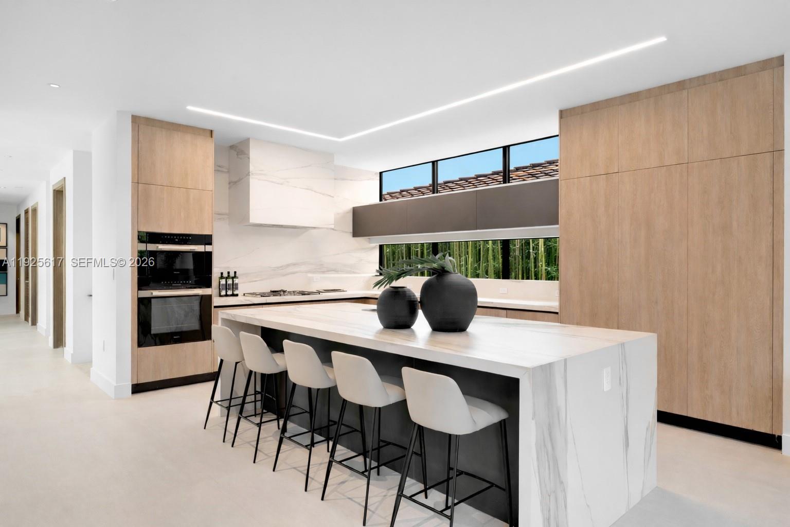 A modern kitchen features a marble-topped island, light wood cabinetry, and a horizontal window — 3551 Crystal Ct, Miami FL 33133, MIAMI, FL