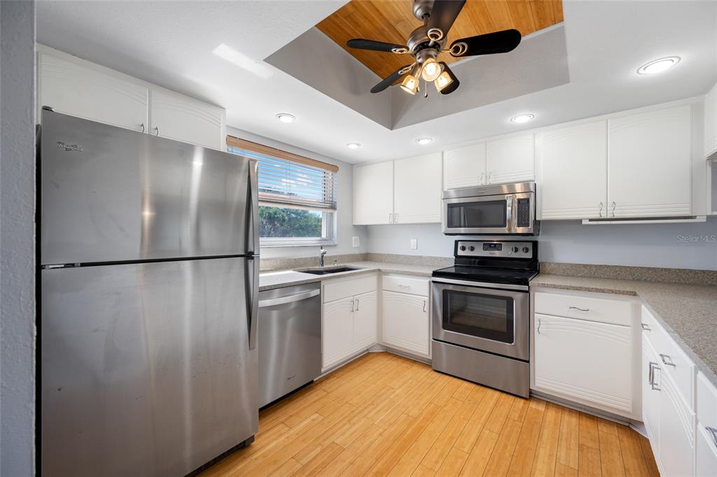 A kitchen features stainless steel appliances, white cabinets, light countertops, and wood flooring — 12424 CAPRI CIRCLE N UNIT 5, TREASURE ISLAND, FL