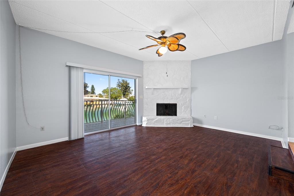 A living room with dark wood floors, a white stone fireplace, and a sliding glass door — 12424 CAPRI CIRCLE N UNIT 5, TREASURE ISLAND, FL