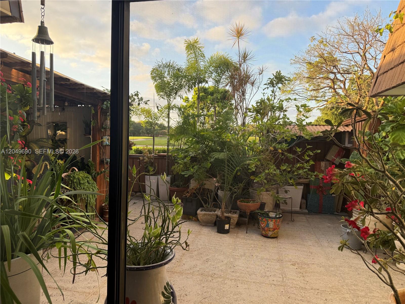 A patio filled with numerous potted plants and trees is viewed through a screen door — 9101 SW 19th Pl # C, Davie FL 33324, DAVIE, FL