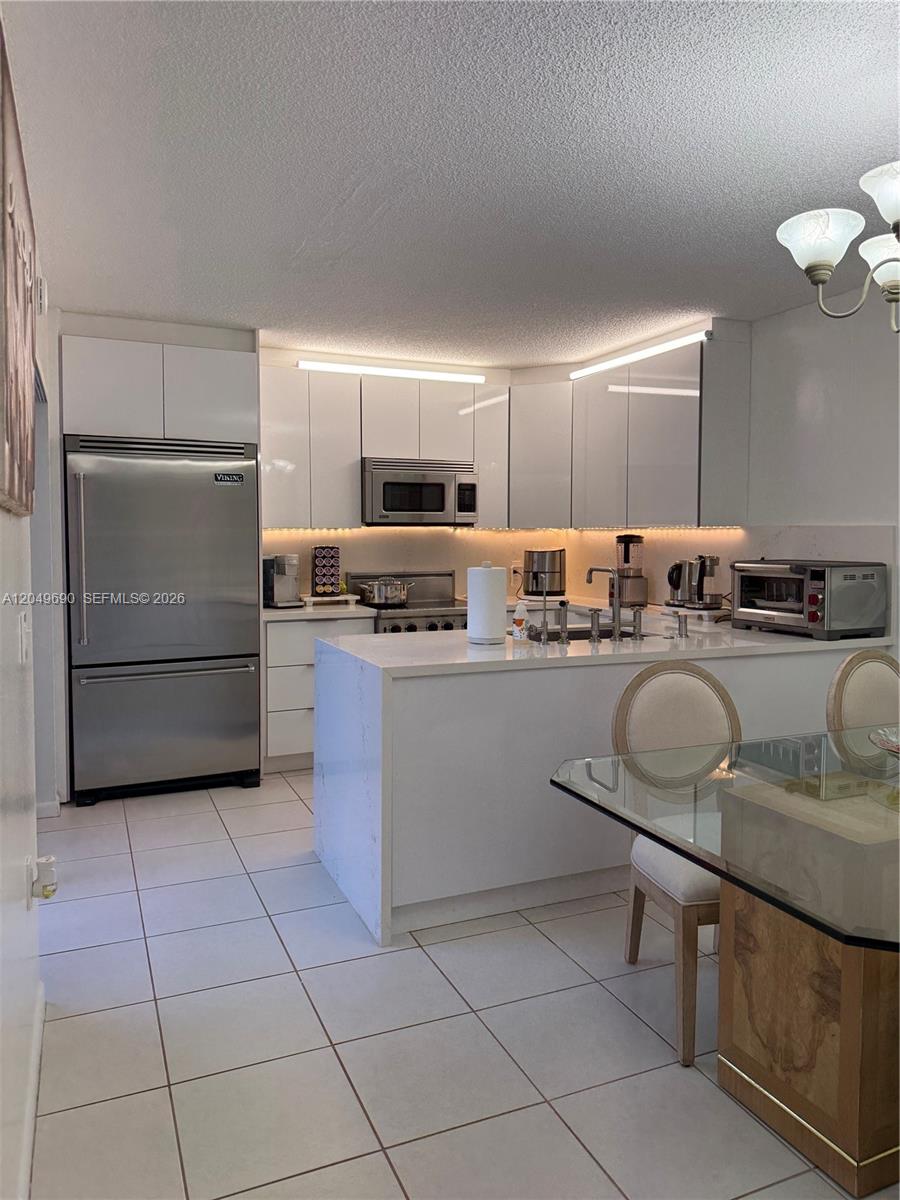 A modern white kitchen features stainless steel appliances, a breakfast bar, and tile flooring — 9101 SW 19th Pl # C, Davie FL 33324, DAVIE, FL