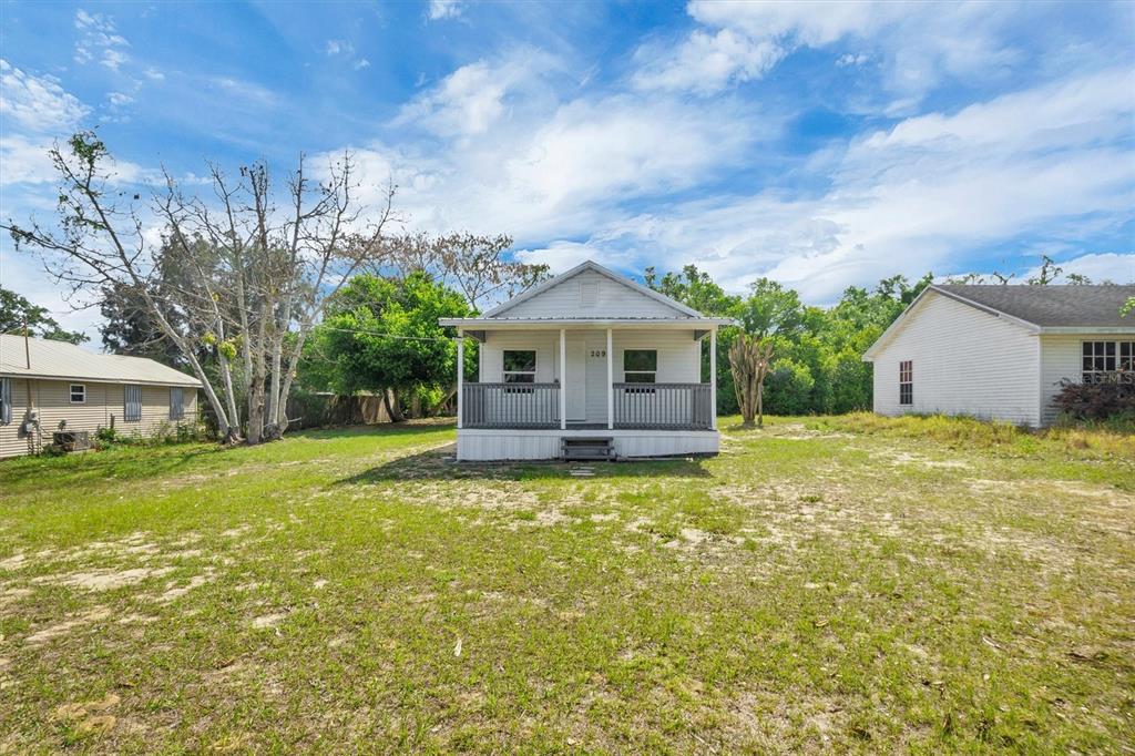 A small white house with a front porch sits on a large, grassy lot — 209 PINEY AVENUE, LAKE WALES, FL