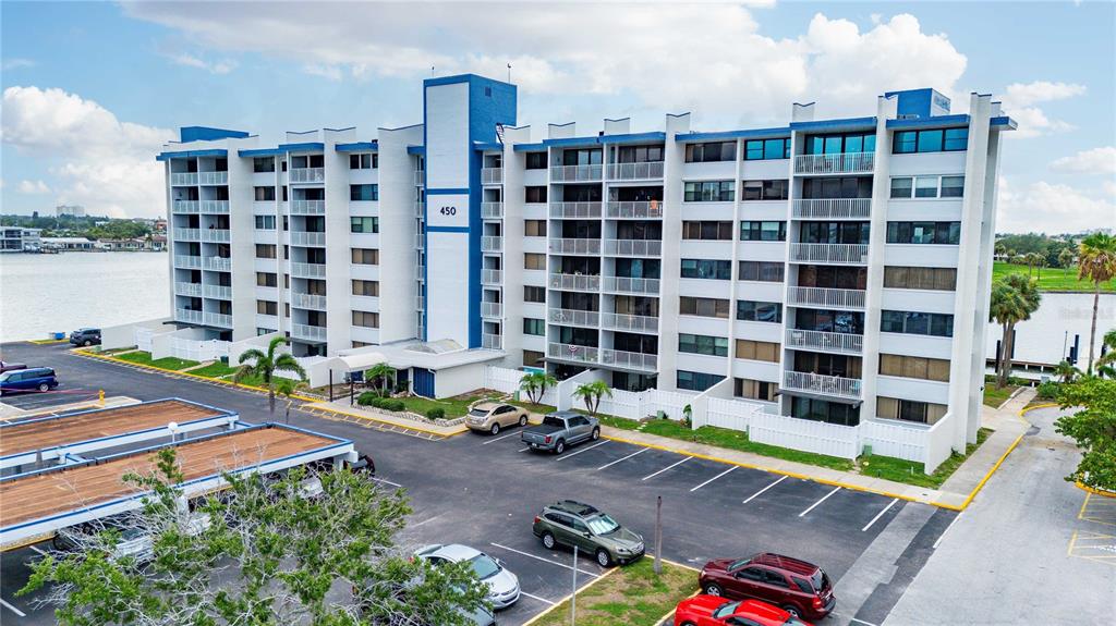An aerial view shows a multi-story apartment building with balconies and an adjacent parking lot — 450 TREASURE ISLAND CAUSEWAY UNIT 311, ST PETERSBURG, FL