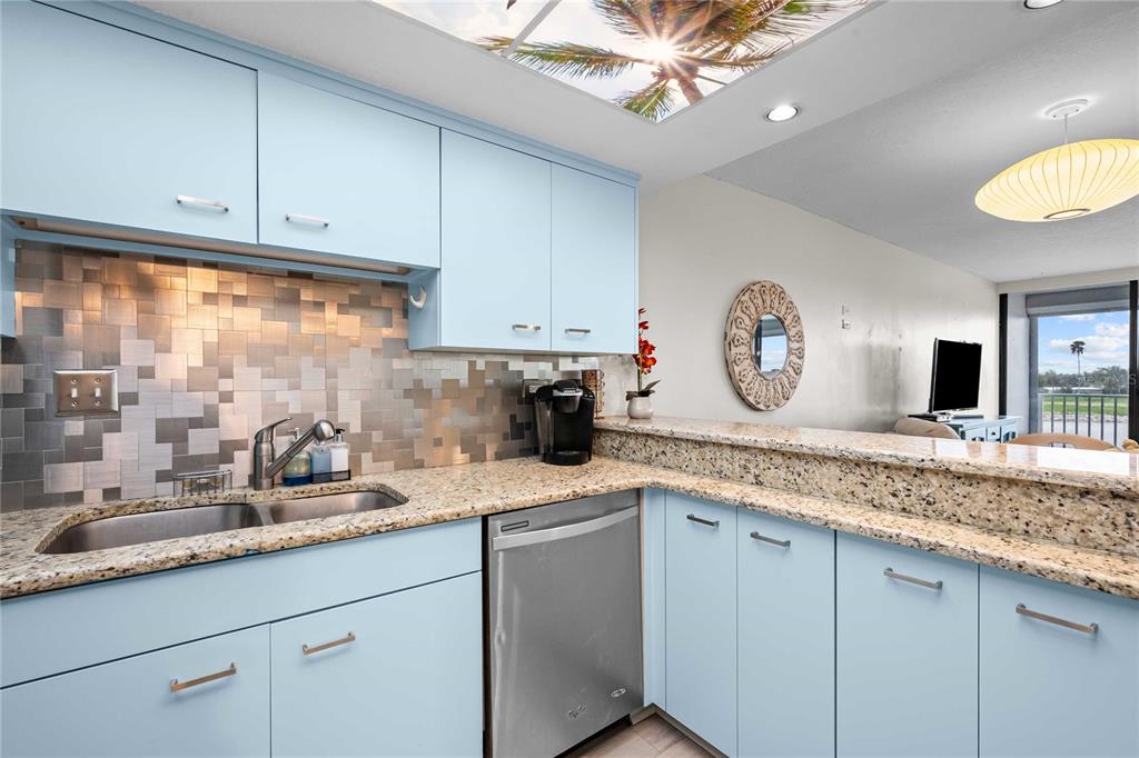 A kitchen features light blue cabinets, granite countertops, a metallic tile backsplash, and stainless steel appliances — 450 TREASURE ISLAND CAUSEWAY UNIT 311, ST PETERSBURG, FL