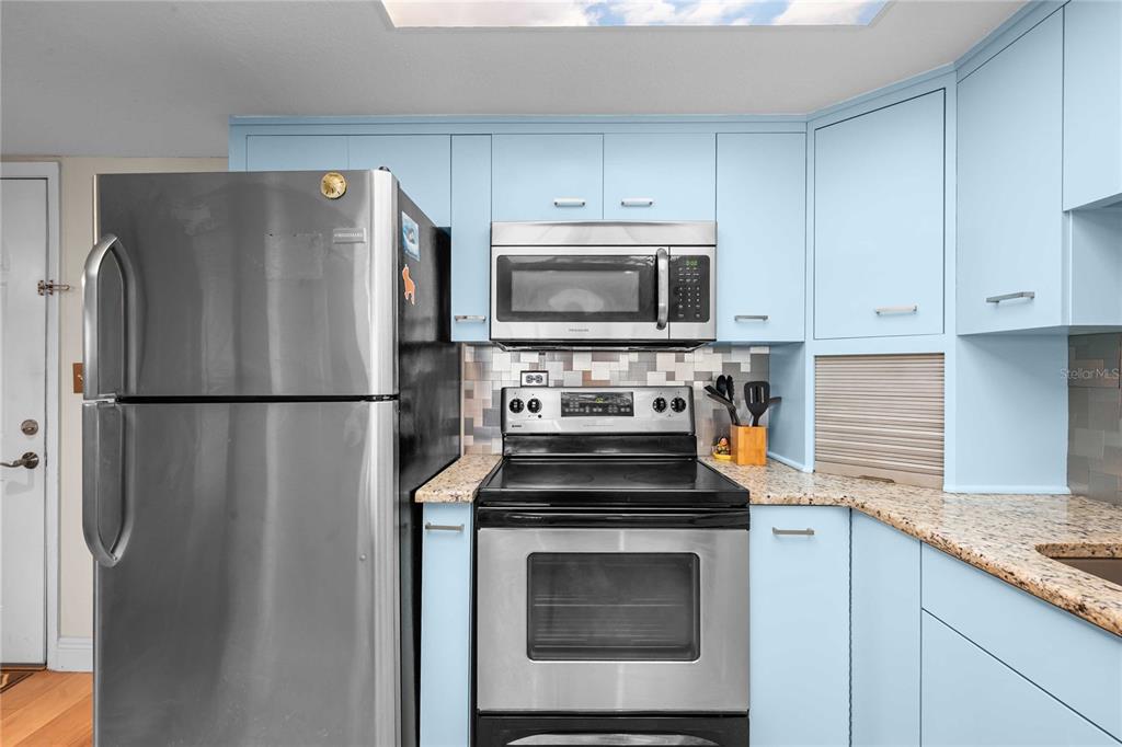 A kitchen features light blue cabinets, stainless steel appliances, and granite countertops — 450 TREASURE ISLAND CAUSEWAY UNIT 311, ST PETERSBURG, FL