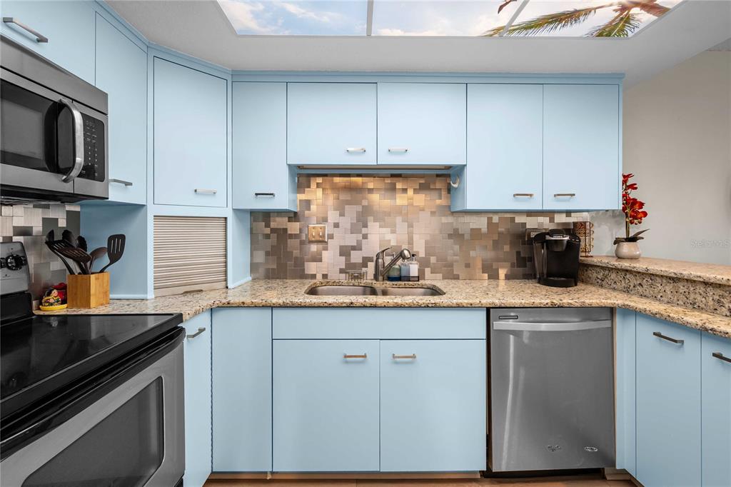 A kitchen features light blue cabinets, granite countertops, a tiled backsplash, and stainless steel appliances — 450 TREASURE ISLAND CAUSEWAY UNIT 311, ST PETERSBURG, FL