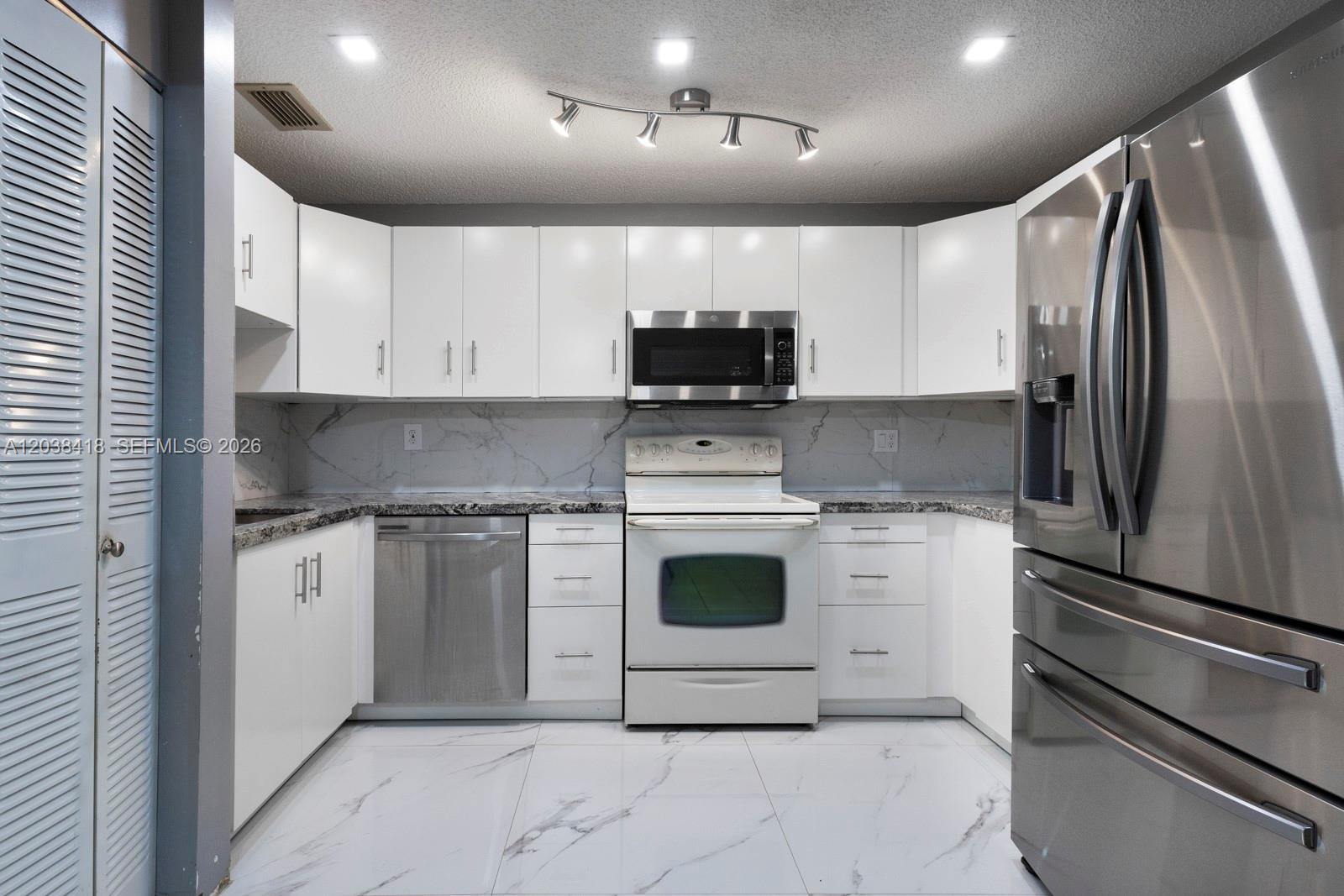 A kitchen features white cabinets, stainless steel appliances, marble-patterned countertops, and matching floor tiles — 12940 SW 64th Ln # 3, Miami FL 33183, MIAMI, FL