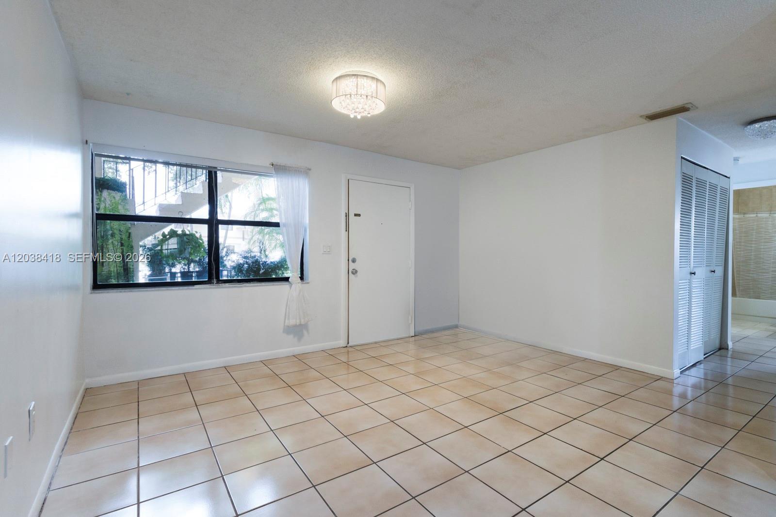 An empty room features white walls, beige tile flooring, a window, and a white door — 12940 SW 64th Ln # 3, Miami FL 33183, MIAMI, FL