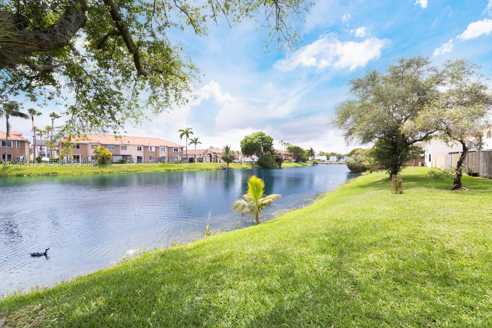 A view of a lake surrounded by green grass, trees, and residential buildings — 12940 SW 64th Ln # 3, Miami FL 33183, MIAMI, FL