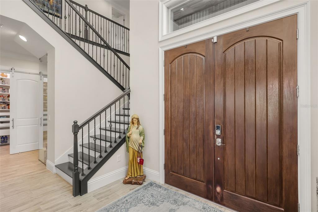 An entryway features a wooden double door, a staircase with black railings, and a statue — 9056 MORGANA COURT, WINTER GARDEN, FL