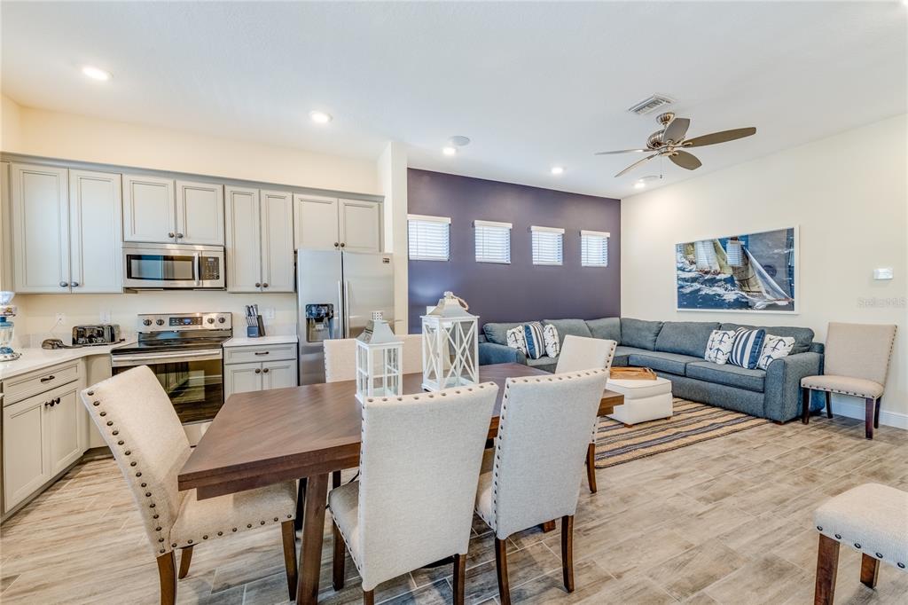 An open-concept kitchen and living area features light gray cabinetry, a dining table, and sectional — 8080 DREAMSICLE DRIVE, KISSIMMEE, FL