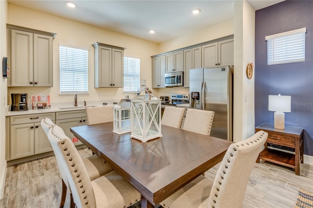 A dining area with a wooden table and chairs sits adjacent to a kitchen with gray cabinets — 8080 DREAMSICLE DRIVE, KISSIMMEE, FL