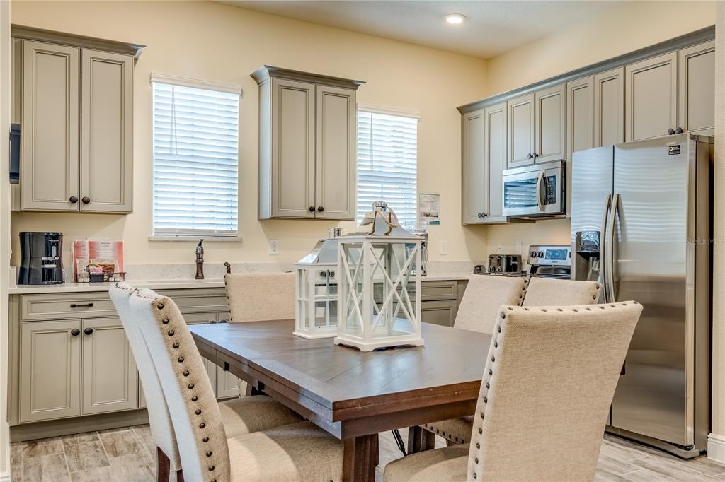 A dining area with a wooden table and upholstered chairs sits before a modern kitchen — 8080 DREAMSICLE DRIVE, KISSIMMEE, FL