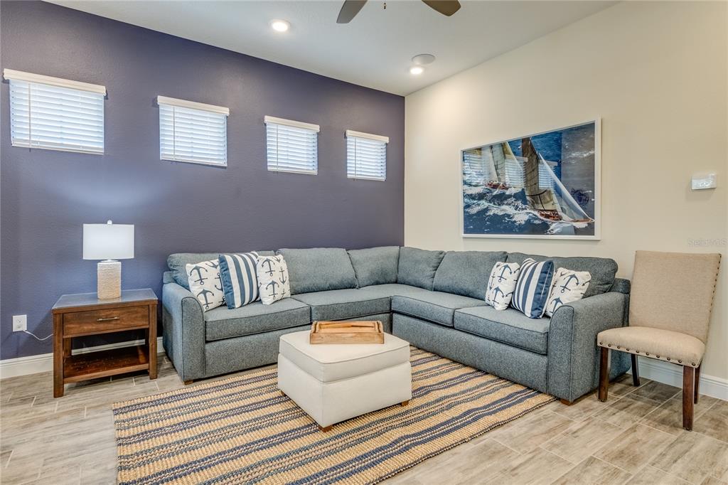 A living room features a blue sectional sofa, a white ottoman, and a nautical-themed painting — 8080 DREAMSICLE DRIVE, KISSIMMEE, FL