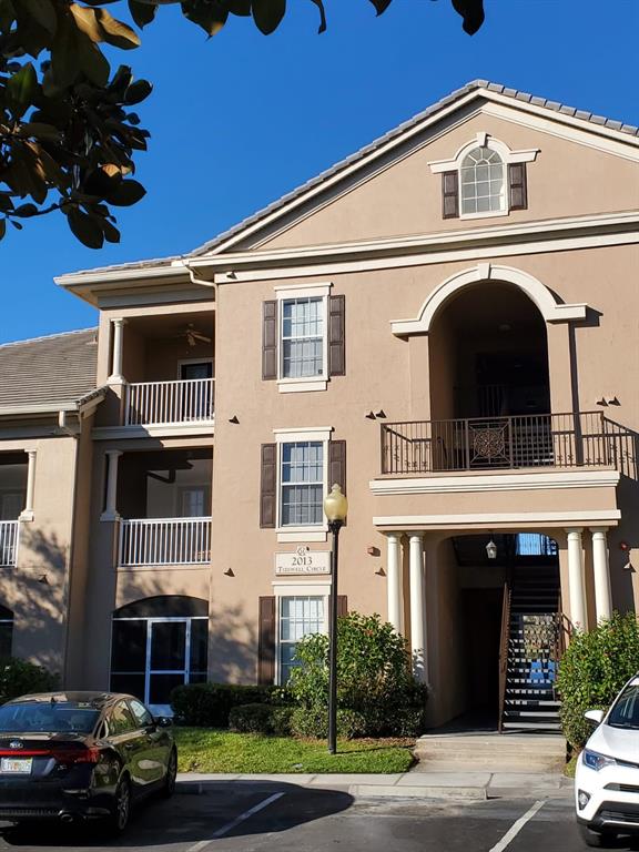 A three-story tan apartment building features balconies, dark shutters, and a covered ground-level entryway — 2013 TIZEWELL CIRCLE UNIT 1403, ORLANDO, FL