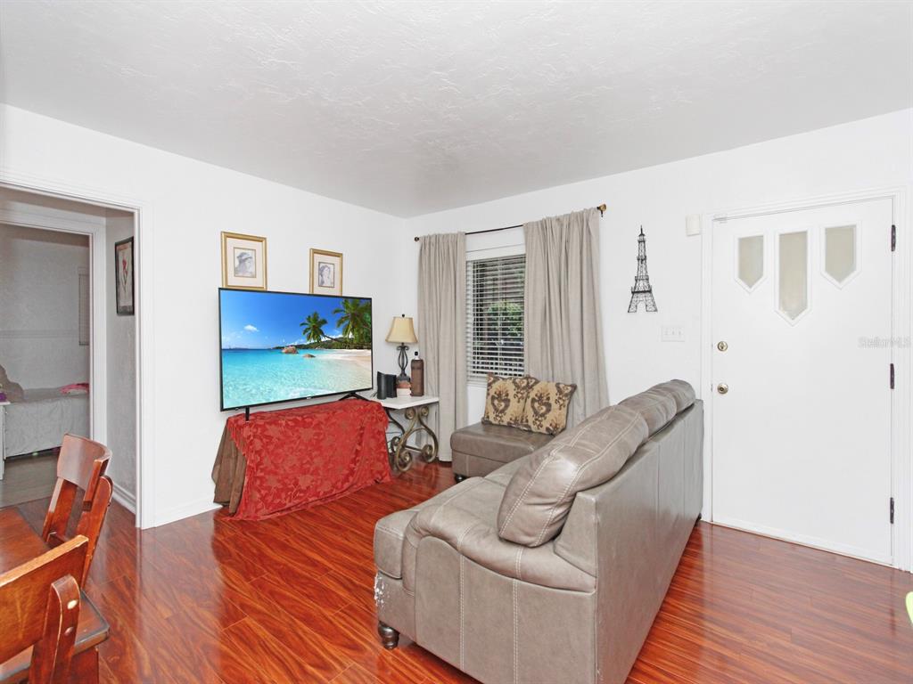 A living room with wood-look flooring, a grey sofa, a television, and a front door — 2541 S PALMETTO AVENUE, SANFORD, FL