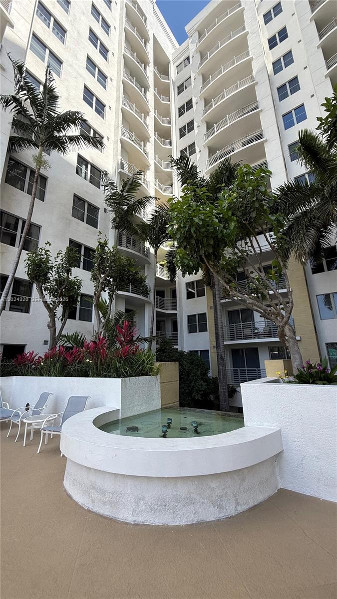 A courtyard features a small circular fountain, potted plants, and white chairs before a tall building — 1830 Radius Dr # 603, Hollywood FL 33020, HOLLYWOOD, FL