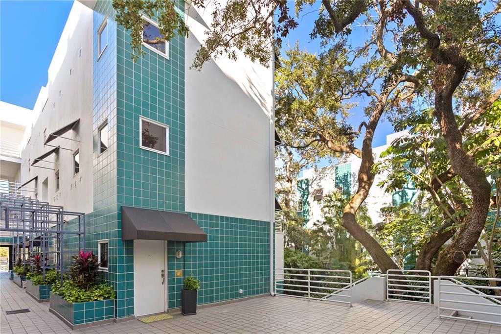 An exterior view of a modern building with teal tiled walls, a white door, and stairs — 4950 BAYSHORE BOULEVARD UNIT 13C, TAMPA, FL