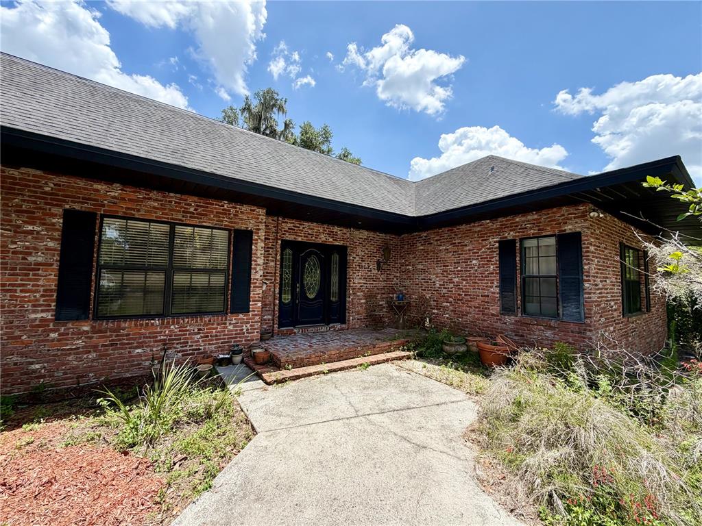 A brick house exterior features a dark front door, black shutters, and a concrete walkway — 1880 HERMOSA AVENUE, BARTOW, FL