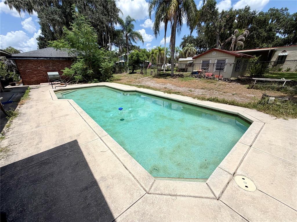 A rectangular swimming pool sits in a backyard with a concrete deck and nearby buildings — 1880 HERMOSA AVENUE, BARTOW, FL