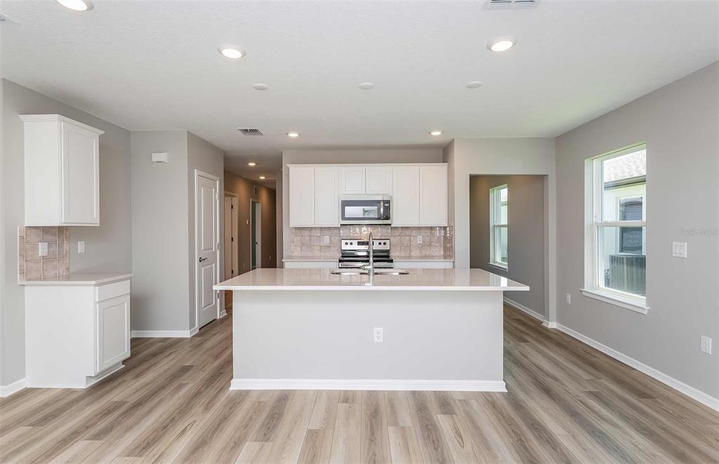A modern kitchen features a central island, white cabinetry, stainless steel appliances, and wood-look flooring — 3027 WINDSWEPT WAY, WILDWOOD, FL