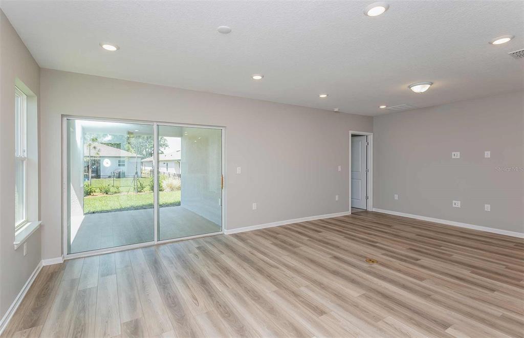 A bright living room features light wood-look flooring, recessed lighting, and sliding glass patio doors — 3027 WINDSWEPT WAY, WILDWOOD, FL