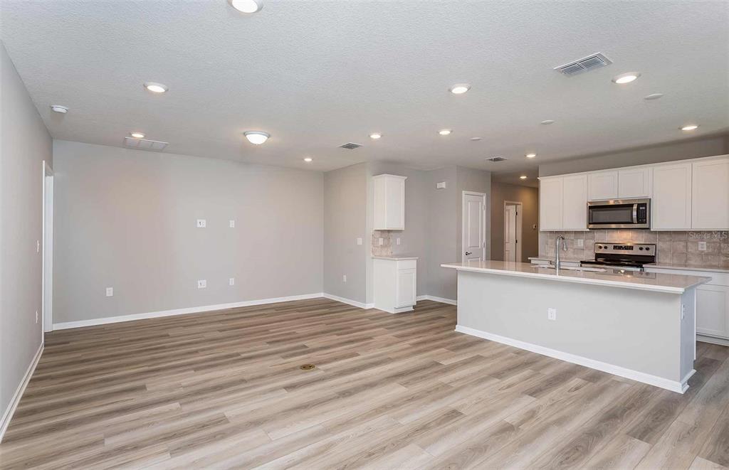 An open-concept kitchen and living area features light wood-look flooring and white cabinetry — 3027 WINDSWEPT WAY, WILDWOOD, FL