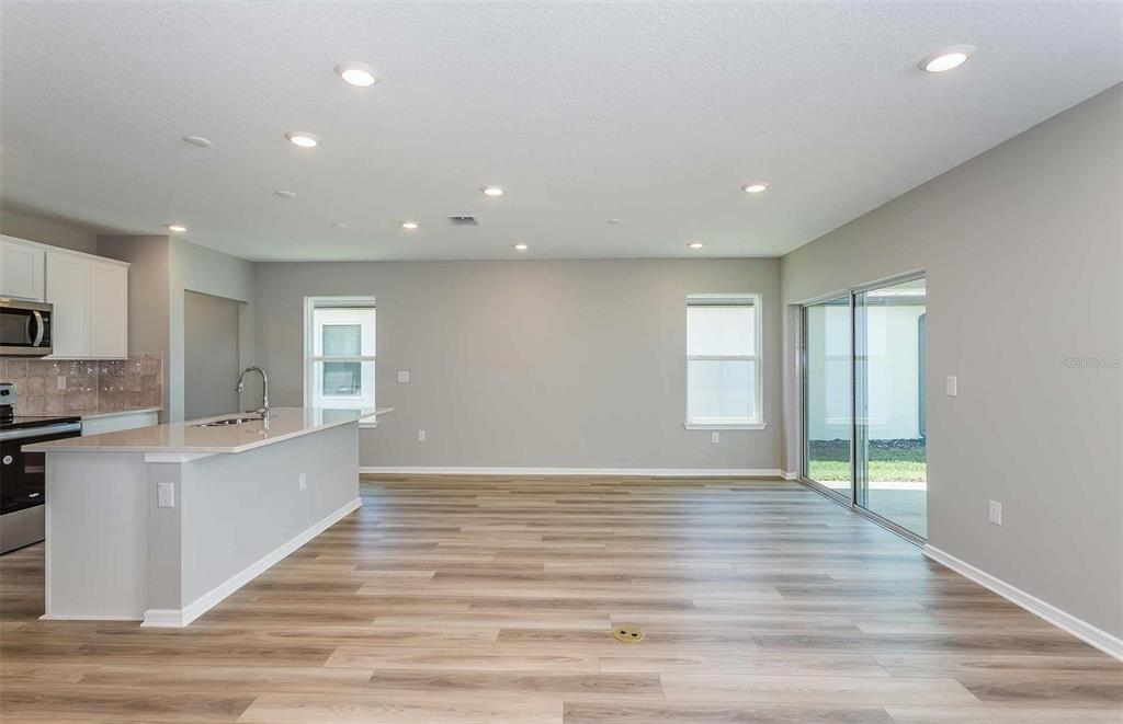 An open-concept kitchen and living area features light wood-look flooring and recessed ceiling lighting — 3027 WINDSWEPT WAY, WILDWOOD, FL