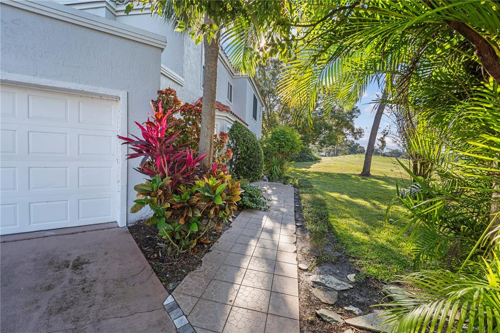 A paved walkway leads past a garage and tropical landscaping toward a grassy golf course — 2649 ALBION AVENUE, ORLANDO, FL