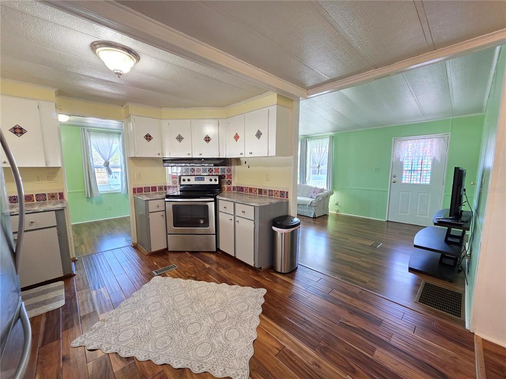 A kitchen with white cabinets, stainless steel appliances, and wood-look flooring opens to a living area — 8027 EASTERN CIRCLE DRIVE, BROOKSVILLE, FL