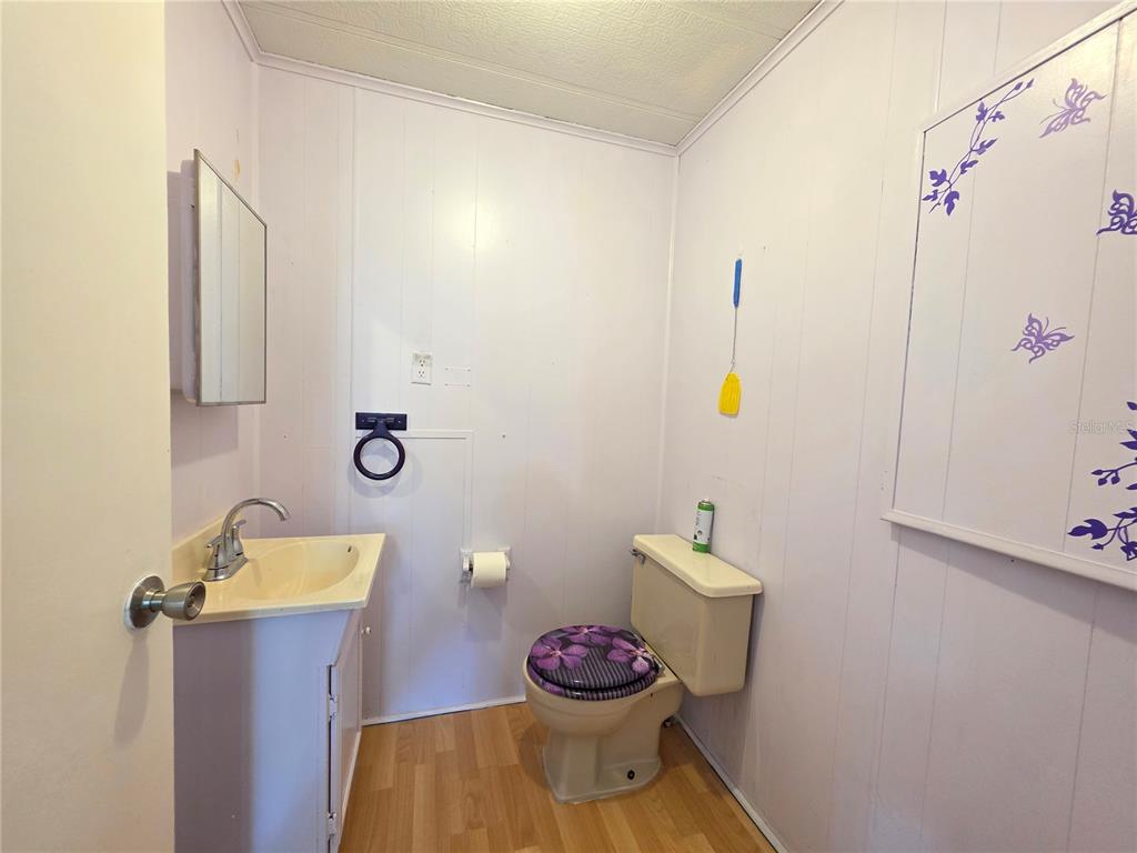 A small bathroom features a vanity sink, toilet with a floral seat, and paneled walls — 8027 EASTERN CIRCLE DRIVE, BROOKSVILLE, FL