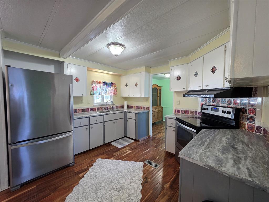 A kitchen features stainless steel appliances, gray lower cabinets, white upper cabinets, and patterned tile — 8027 EASTERN CIRCLE DRIVE, BROOKSVILLE, FL