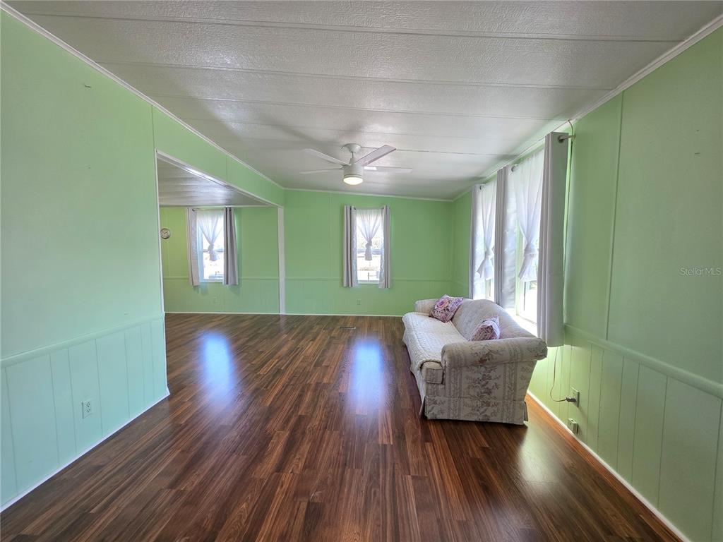 A living room features light green paneled walls, dark wood-look flooring, and a ceiling fan — 8027 EASTERN CIRCLE DRIVE, BROOKSVILLE, FL