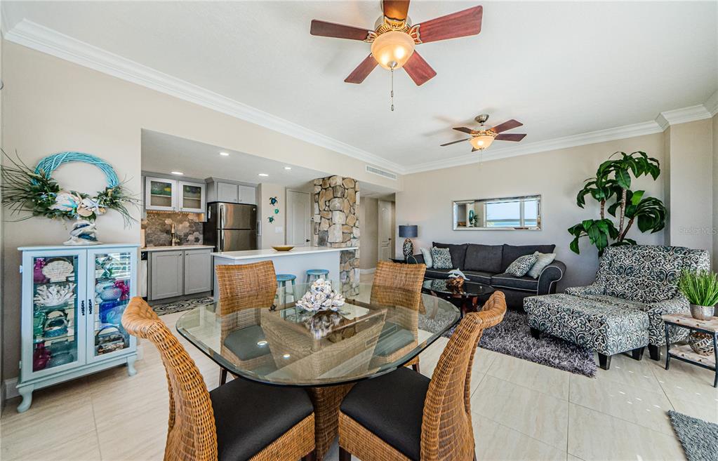 An open-concept living and dining area features a glass table, wicker chairs, and stone accents — 880 MANDALAY AVENUE UNIT S202, CLEARWATER, FL