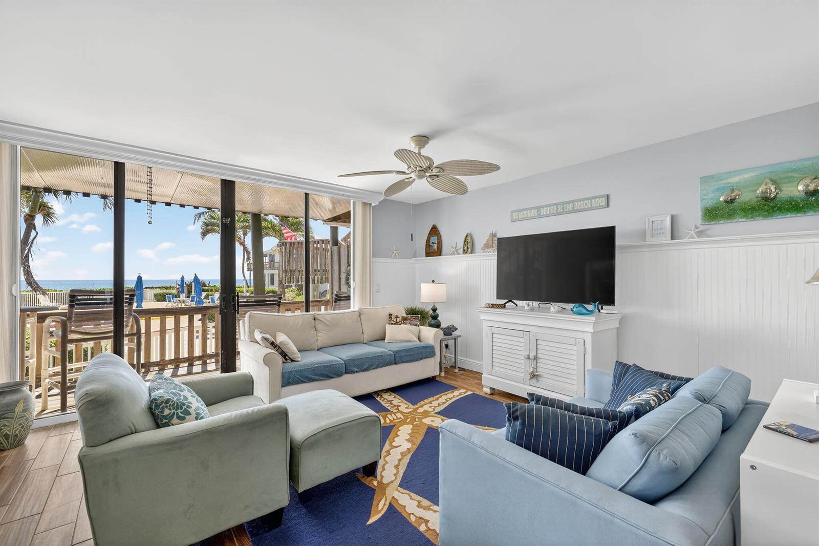 A living room features a beach-themed rug, white wainscoting, and a sliding door to a balcony — 2355 NE Ocean Boulevard # 17a, Stuart FL 34996, STUART, FL