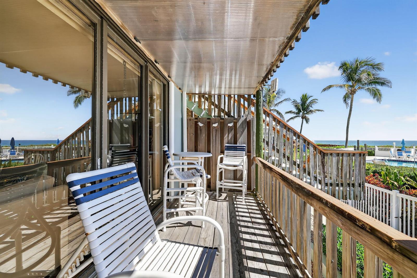 A wooden balcony with white patio furniture overlooks a swimming pool and the ocean — 2355 NE Ocean Boulevard # 17a, Stuart FL 34996, STUART, FL