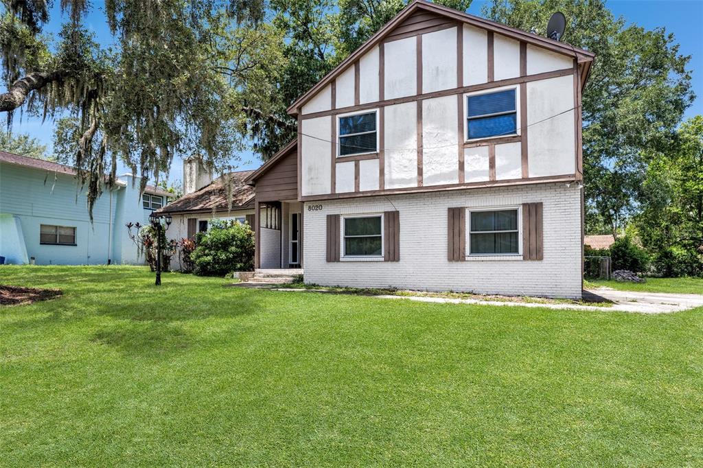 A two-story house with white brick, timber-framed siding, and a front lawn with trees — 8020 TIERRA VERDE DRIVE, TAMPA, FL