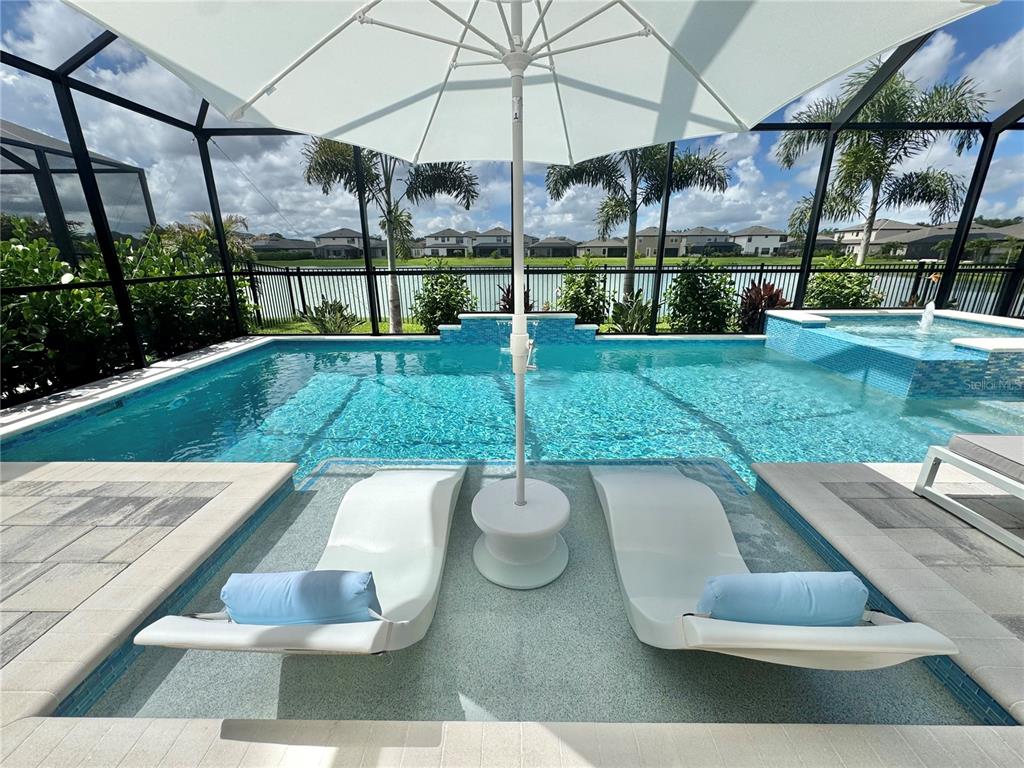 A swimming pool with a sun shelf, lounge chairs, and an umbrella inside a screened enclosure — 13027 HOMESTEAD LANE, PARRISH, FL