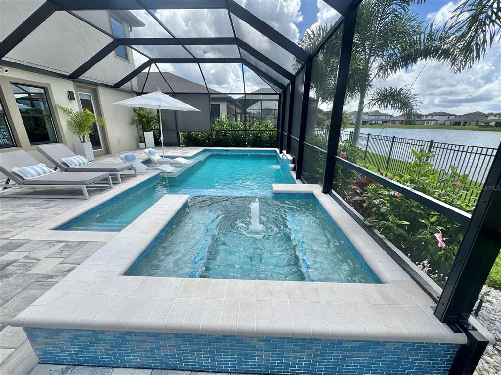 A screened-in pool and spa area with lounge chairs overlooks a lake — 13027 HOMESTEAD LANE, PARRISH, FL
