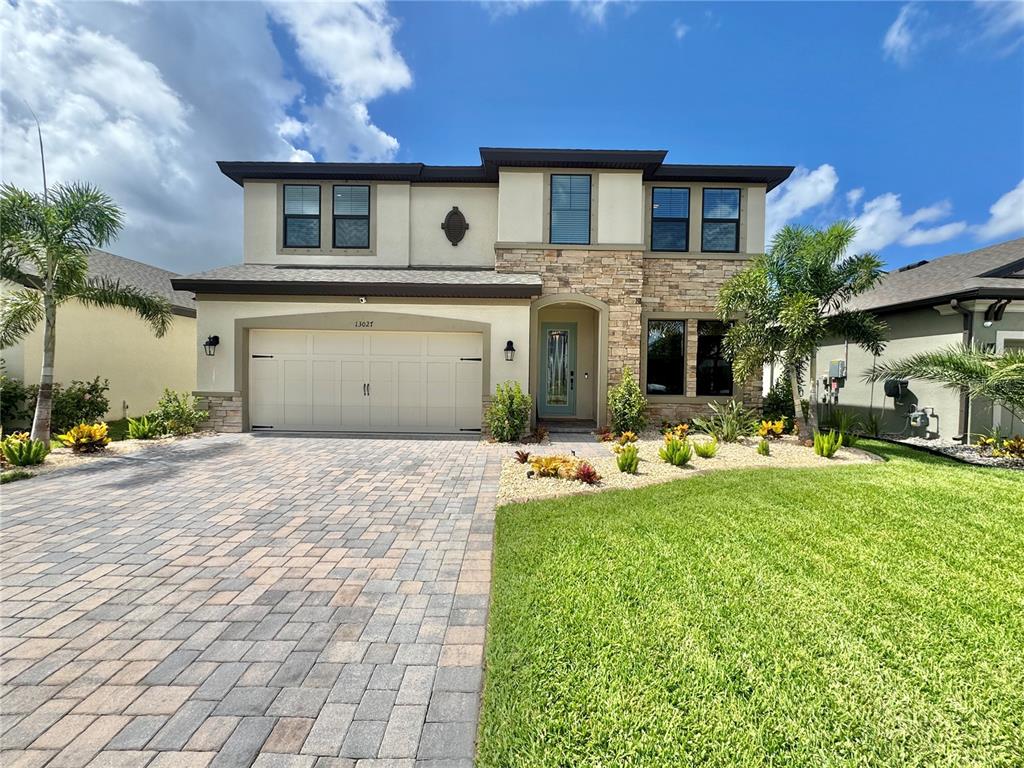 A two-story house with a stone facade, a paved driveway, and a manicured front lawn — 13027 HOMESTEAD LANE, PARRISH, FL