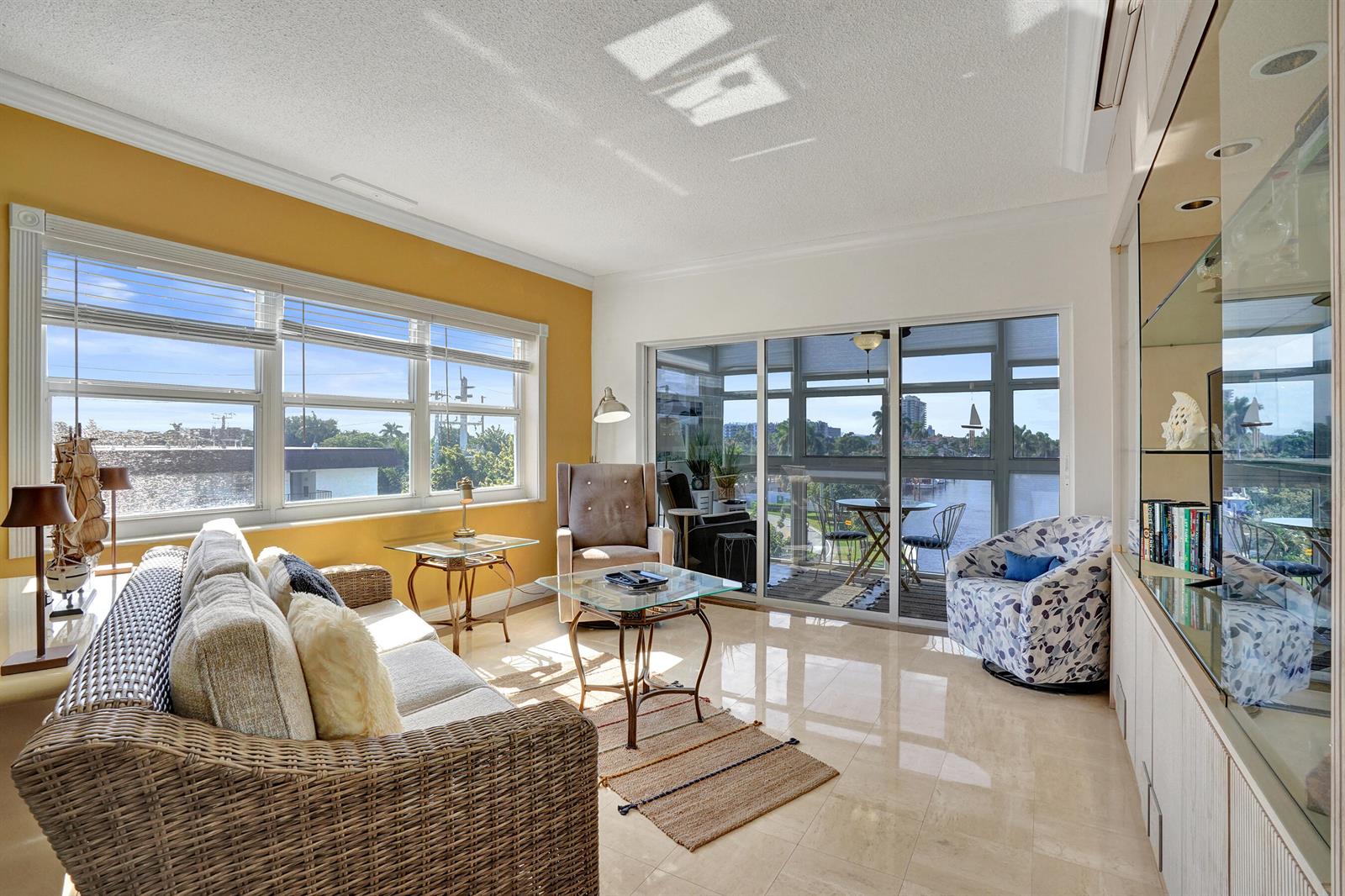 A sunlit living room features wicker furniture, a glass coffee table, and a balcony view — 1481 S Ocean Boulevard # 412, Pompano Beach FL 33062, POMPANO BEACH, FL