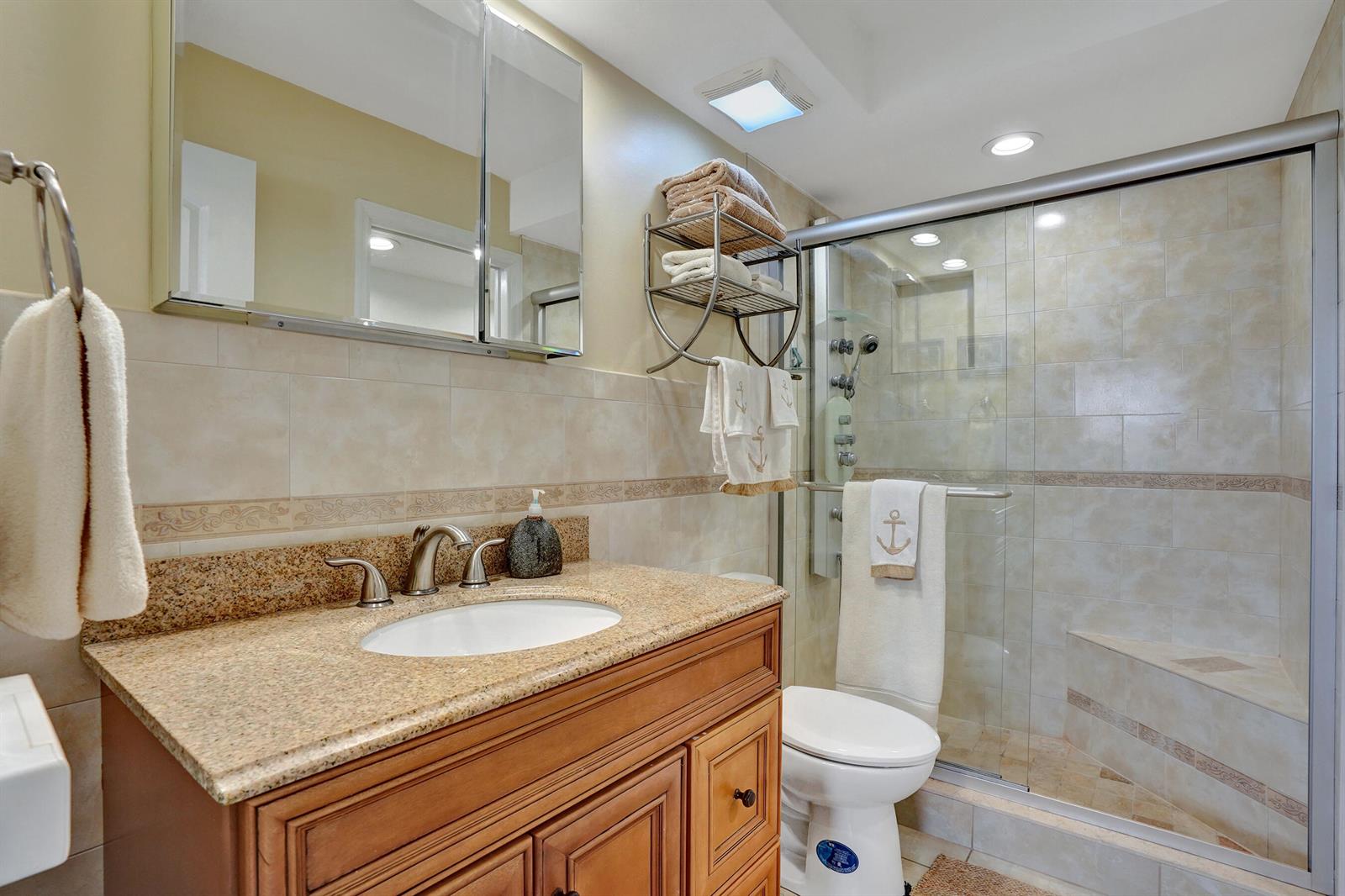 A bathroom features a granite vanity, wooden cabinet, glass-enclosed shower, and a toilet — 1481 S Ocean Boulevard # 412, Pompano Beach FL 33062, POMPANO BEACH, FL