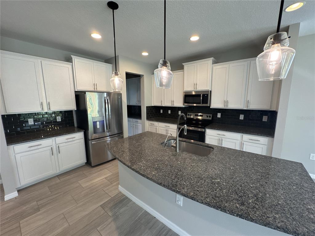 A kitchen features white cabinets, dark granite countertops, stainless steel appliances, and a central island — 6356 MIGHTY EAGLE WAY, SARASOTA, FL