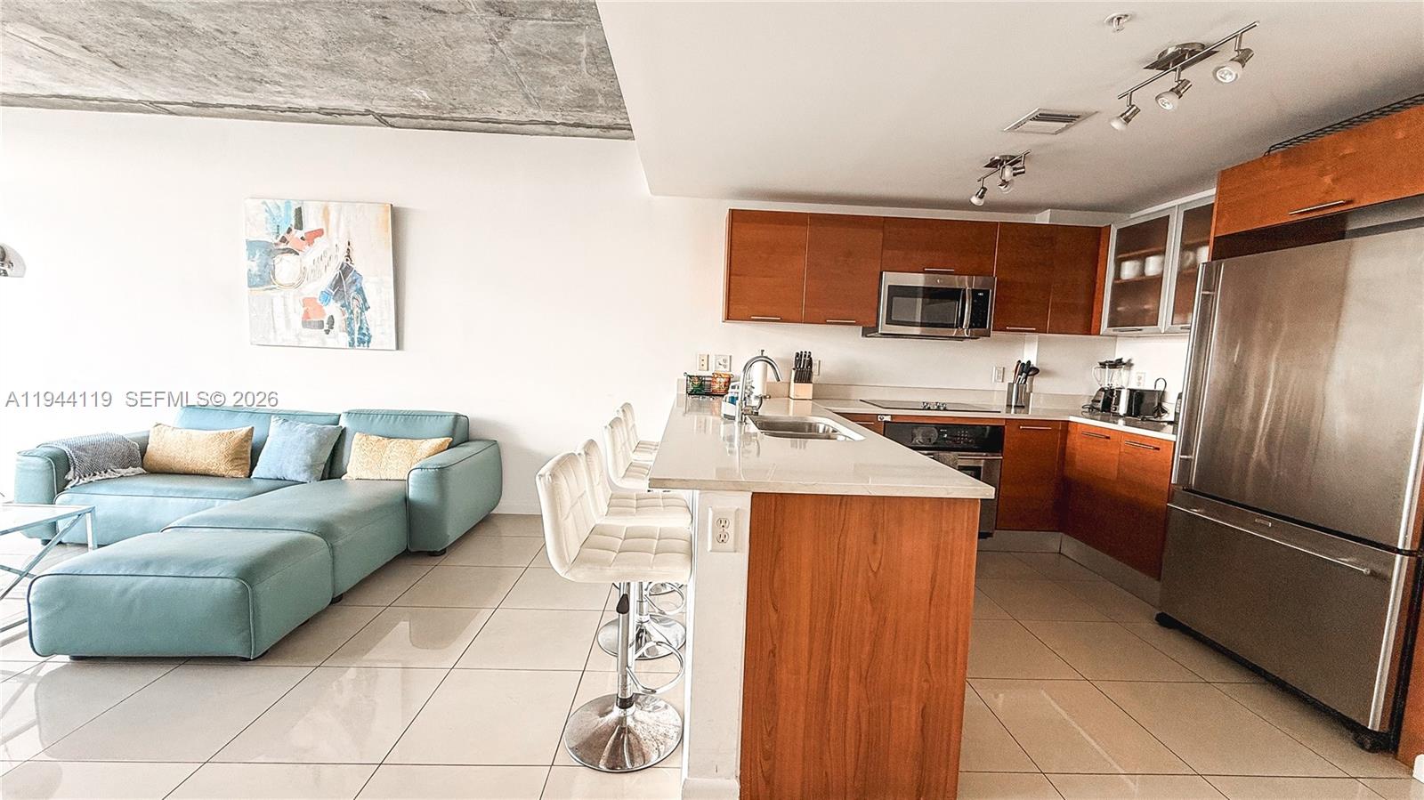 An open-concept kitchen with wood cabinets and a breakfast bar overlooks a living area — 3250 NE 1st Ave # 1110, Miami FL 33137, MIAMI, FL