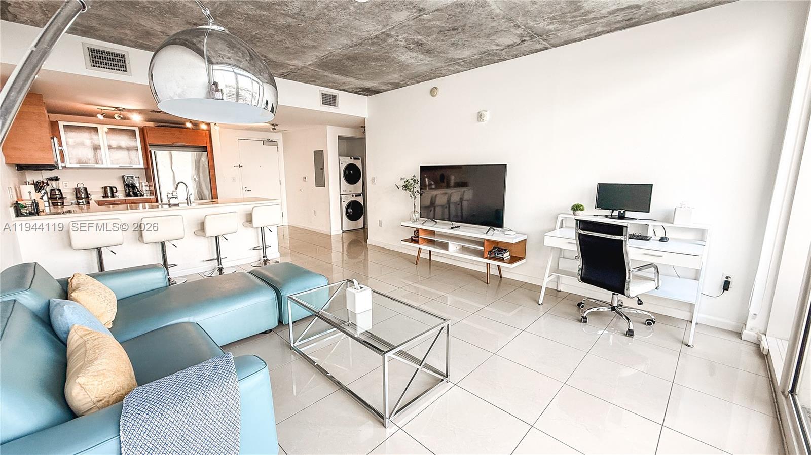A modern living room features a blue sectional, glass coffee table, and an open kitchen — 3250 NE 1st Ave # 1110, Miami FL 33137, MIAMI, FL