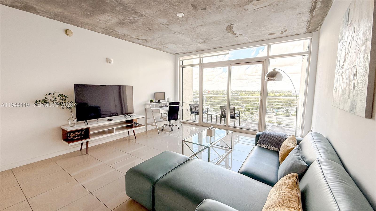 A modern living room features a concrete ceiling, tiled floors, and a balcony with views — 3250 NE 1st Ave # 1110, Miami FL 33137, MIAMI, FL