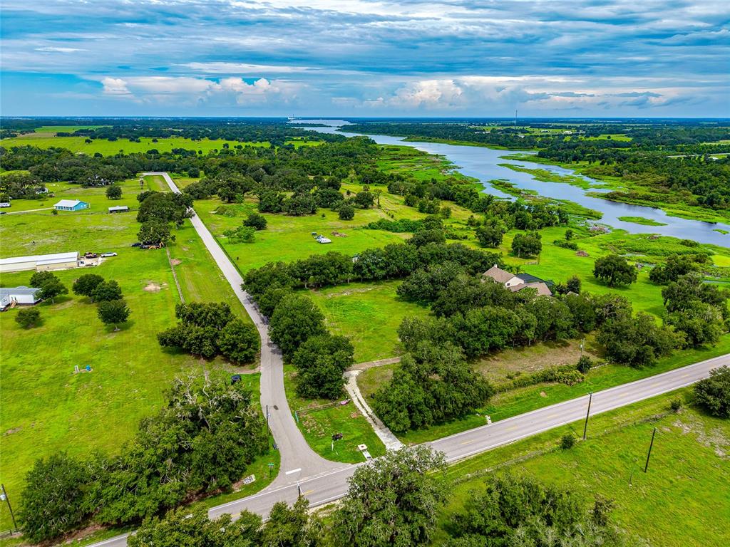 An aerial view shows a rural property with a road, green fields, and a river — 26207 39TH PLACE E, MYAKKA CITY, FL