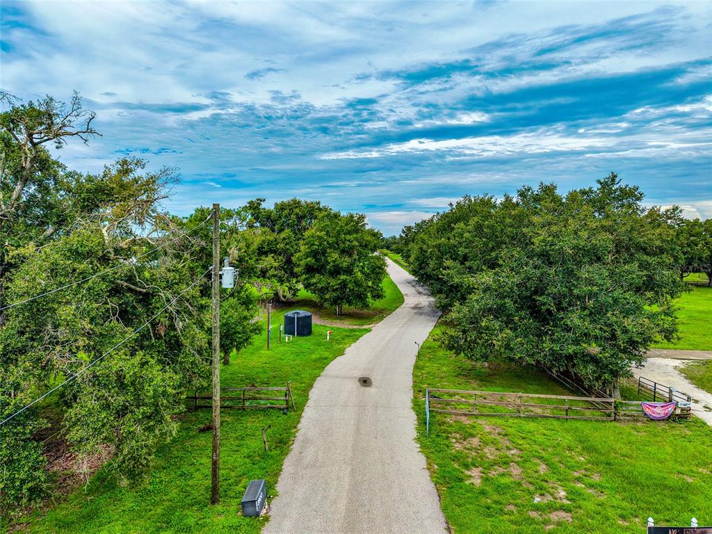 An aerial view shows a paved driveway leading through a grassy area with mature trees — 26207 39TH PLACE E, MYAKKA CITY, FL