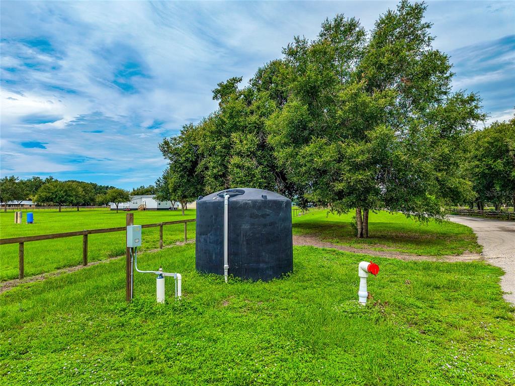 A large black water storage tank sits in a grassy field near a gravel driveway — 26207 39TH PLACE E, MYAKKA CITY, FL